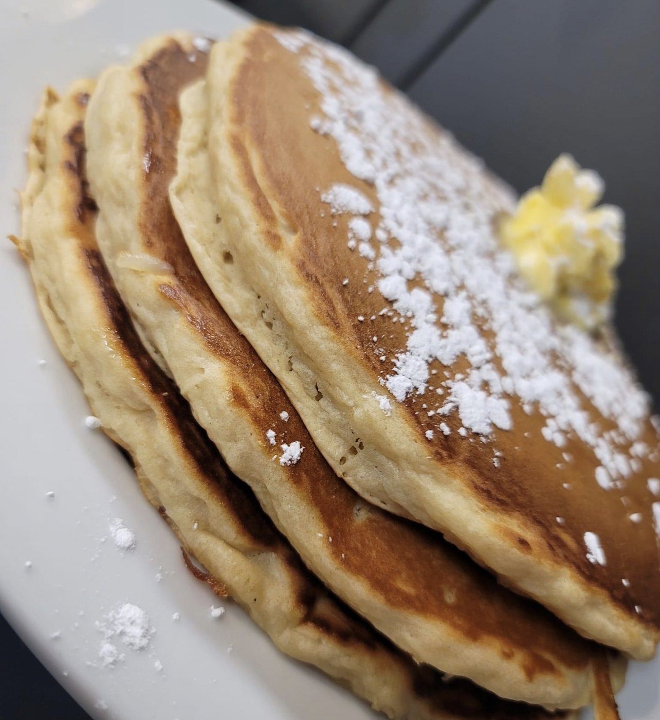 Stack of pancakes topped with powdered sugar and butter