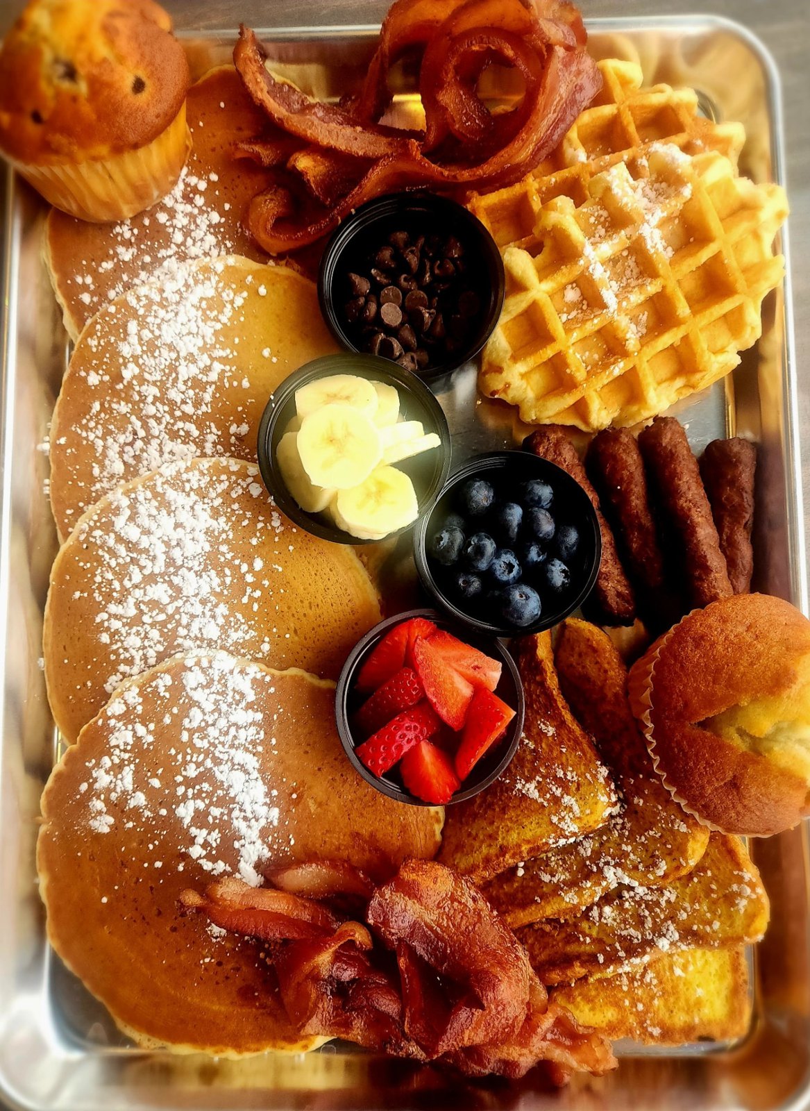 Breakfast charcuterie board with pancakes, waffle, bacon and fruit