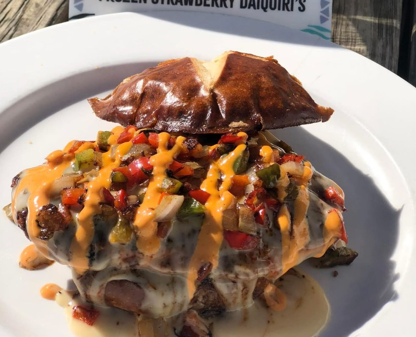 Tex Mex smash burger with sautéed peppers, onions and queso on a pretzel bun